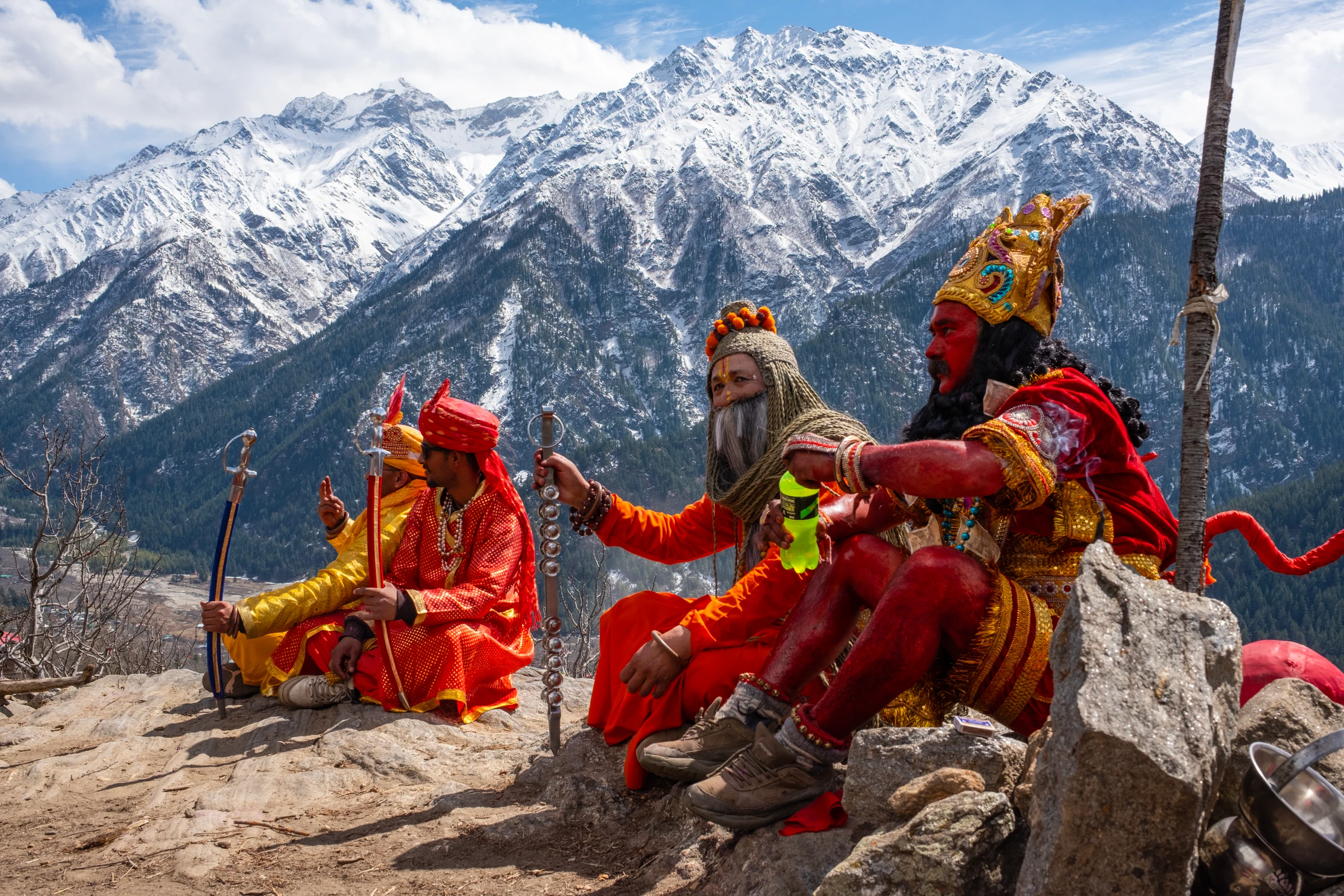 Costumed festival participants seated on rocks in front of snow-covered mountains