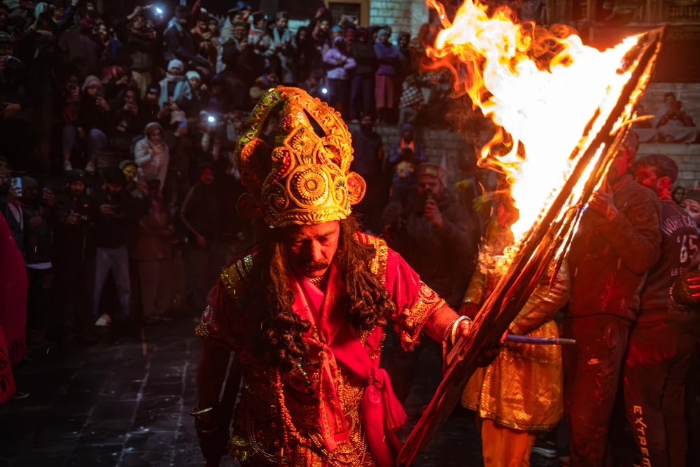 A crowned festival participant carrying flaming torches through a crowd at night.