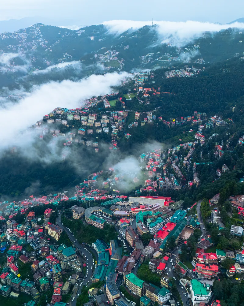 Winding roads and colourful hillside buildings surrounded by forest and mist.