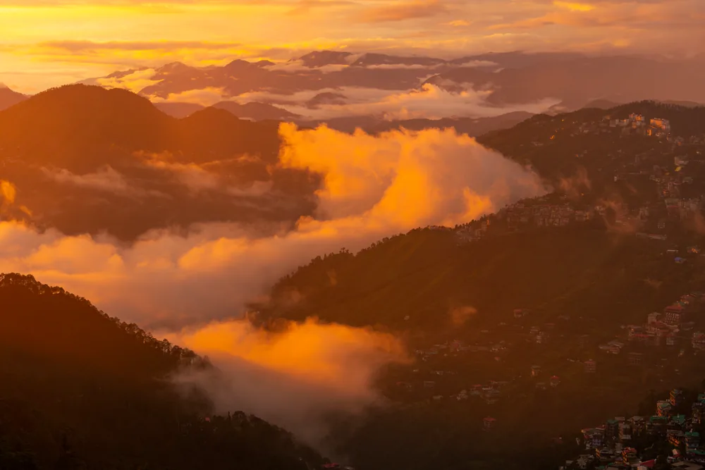 Golden sunset light illuminating clouds between dark mountain ridges.