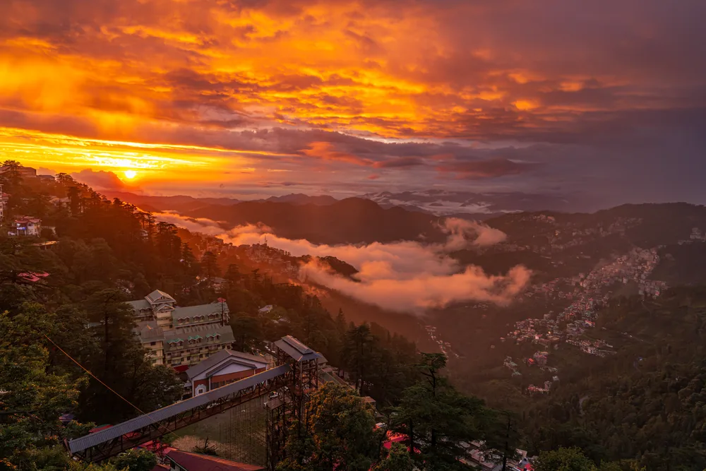 An orange sunset above mist-filled valleys and hillside buildings.