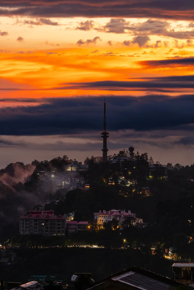 An orange evening sky above a hilltop tower and layers of cloud.